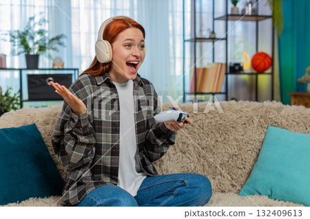 Young woman on sofa playing video game with joystick emotionally reacting to action on screen 132409613