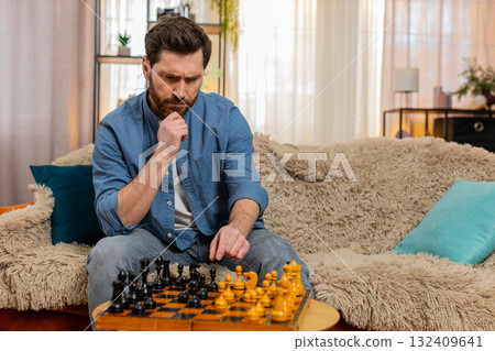 Young man playing chess alone making serious move deep thinking strategy concentration home sofa Young man playing chess alone making serious move deep thinking strategy concentration home sofa 132409641