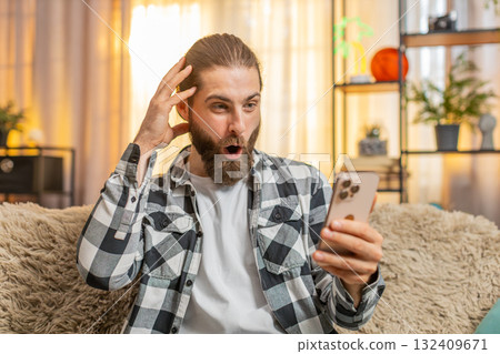 Young man typing fast at home, smartphone deal hunt, excitement, sudden wow, big online find 132409671