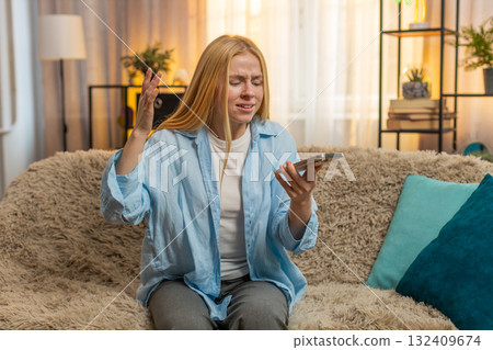 Young woman on loudspeaker call, emotional argument escalates, frustrated end tense home sofa moment Young woman on loudspeaker call, emotional argument escalates, frustrated end tense home sofa moment 132409674