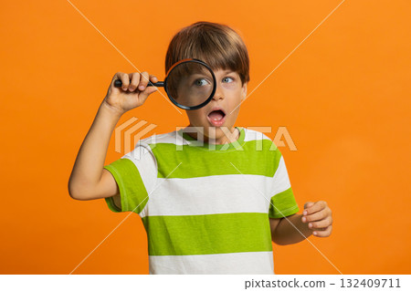 Child boy kid holds magnifying glass near face looking at camera with big zoomed eye, analyzing Child boy kid holds magnifying glass near face looking at camera with big zoomed eye, analyzing 132409711