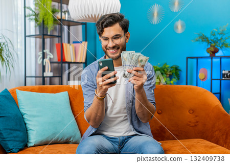 Rich happy Indian man counting money cash on smartphone calculator app, calculate income earnings Rich happy Indian man counting money cash on smartphone calculator app, calculate income earnings 132409738