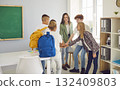 Happy school children with teacher standing in the classroom putting their hands in stack together. 132409803