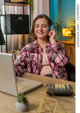 Excited business woman listening music through wireless headphones sitting at home office desk Excited business woman listening music through wireless headphones sitting at home office desk 132409867