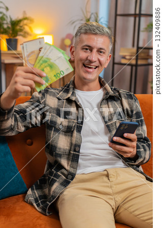Smiling happy Caucasian man counting money euro cash use smartphone income salary lottery game win 132409886