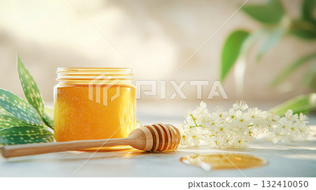 Natural rustic honey jar with hexagonal texture glows linden blossom, decorated with white blossoms and wooden spoon. 132410050