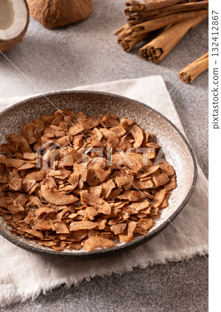 Coconut chips with cinnamon in glass jar on gray background. Healthy sugar free dessert. Vertical format. Sri lankan local snack. 132412867