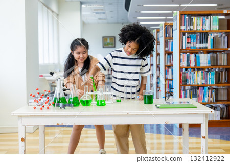 Wide shot two girls enjoy to study with science experiment by mix green solution with test tube in area of public library. 132412922
