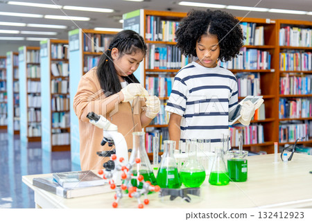 Close up two girls enjoy to study with science experiment by mix green solution with test tube in area of public library. 132412923