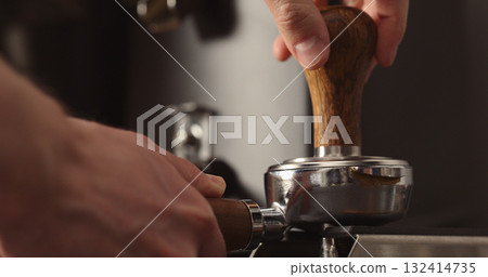 man tamping freshly ground coffee in portafilter 132414735