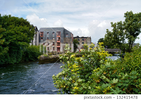 Picturesque scene in Ireland, with a river flowing through a town with stone buildings and lush greenery. 132415478