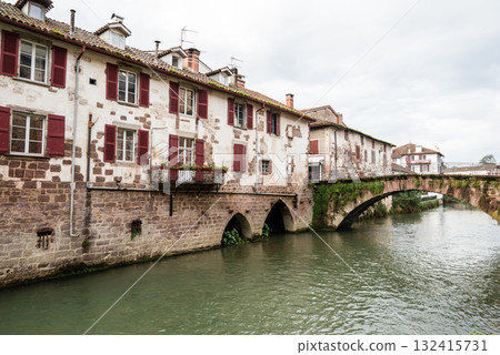 Historic buildings and trees along the river in the morning mist in Saint-Jean-Pied-de-Port, Basque Country, France 132415731