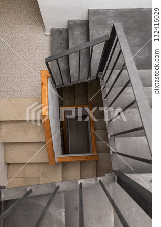 A modern spiral staircase with wooden and concrete elements. The view is from above, showcasing the unique design and materials used in the construction. A modern spiral staircase with wooden and concrete elements. The view is from above, showcasing the unique design and materials used in the construction. 132416029