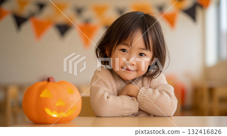 秋天萬聖節的室內，一個大約 2 歲的女孩將手臂放在桌子上，微笑著 132416826