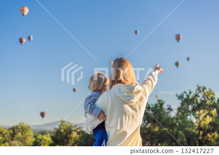 Mother with her young son as tourists, standing with colorful hot air balloons floating behind them over Teotihuacan, Mexico. Family travel, adventure, and cultural exploration concept 132417227