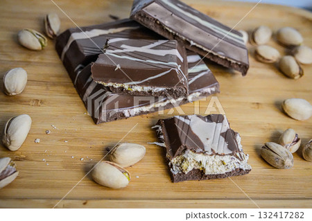 Medium shot of broken chocolate pieces with whole pistachios scattered around. Perfect for food photography, desserts, confectionery, healthy snacks, and gourmet concepts. 132417282