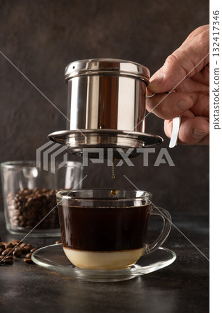 Brew Vietnamese coffee with sweet condensed milk in glass cup by traditional method on black background. Close up. Brew Vietnamese coffee with sweet condensed milk in glass cup by traditional method on black background. Close up. 132417346