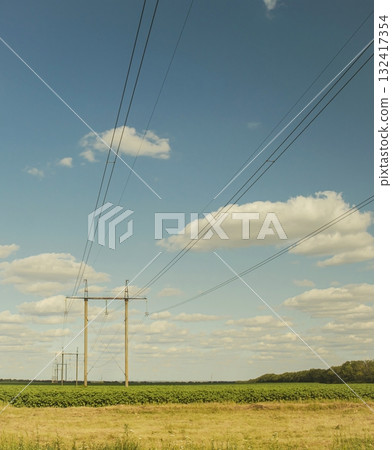 Power lines and power line pylons, electrical wires stretch across the rural landscape. Power lines stretch across a green field under a blue sky. Power lines and power line pylons, electrical wires stretch across the rural landscape. Power lines stretch across a green field under a blue sky. 132417354