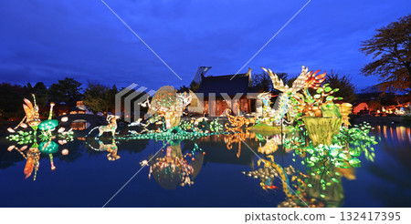 Chinese Garden illuminated at night with colorful figurines reflected on water, Chinese Pavilion and Stadium tower 132417395