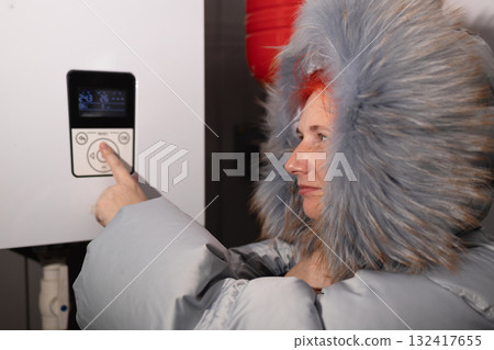 Woman in Winter Clothes Adjusts the Heating System Thermostat at Home 132417655