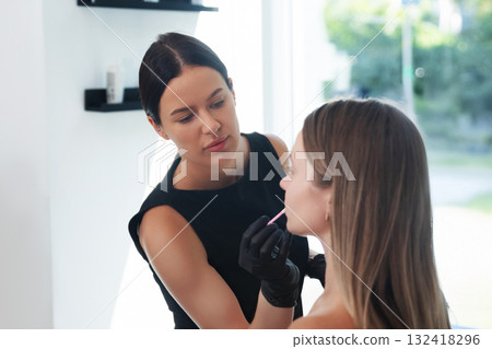 Makeup artist applying lipstick to a client in a bright beauty studio during daytime 132418296