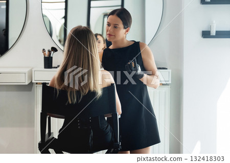 Beauty professional applying makeup to client in modern salon during bright afternoon 132418303