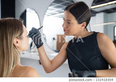 Makeup artist applying makeup to a client in a modern beauty studio during a daytime session 132418304