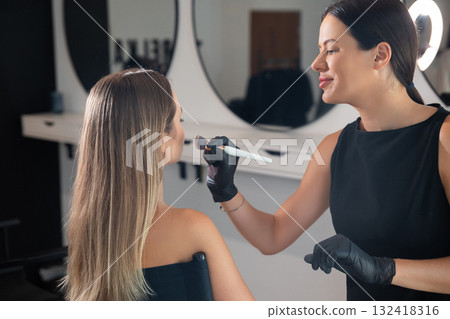 Professional makeup artist applying cosmetics in a modern salon with mirrors and good lighting Professional makeup artist applying cosmetics in a modern salon with mirrors and good lighting 132418316