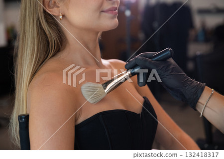 Makeup artist applying bronzer to a woman shoulders in a beauty studio during a daytime beauty session Makeup artist applying bronzer to a woman shoulders in a beauty studio during a daytime beauty session 132418317