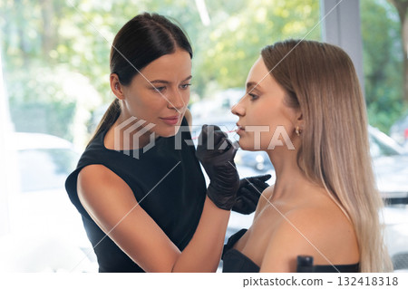 Makeup artist applying cosmetic products to a model's face during a beauty session in a bright studio setting 132418318