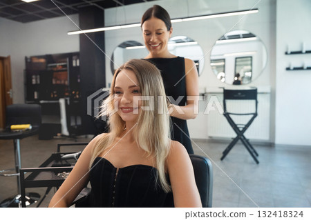 Professional hairstylist creates a beautiful look for a smiling client in a modern salon during the daytime 132418324