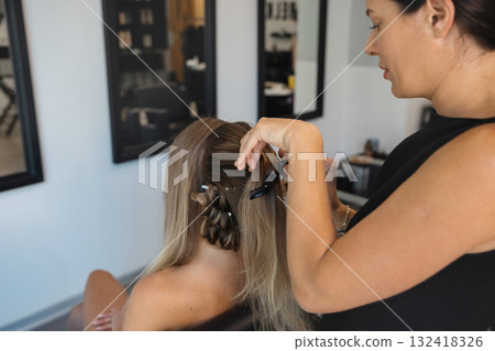 Hair stylist arranging long hair for a client in a modern salon during daylight hours Hair stylist arranging long hair for a client in a modern salon during daylight hours 132418326