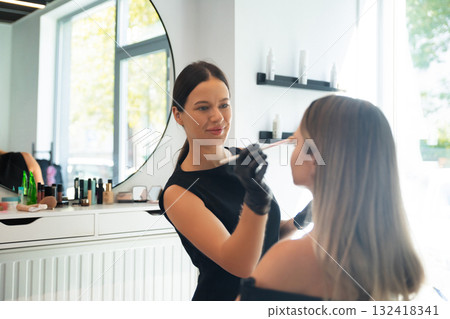 Makeup artist applies makeup to client in a modern beauty salon during daytime Makeup artist applies makeup to client in a modern beauty salon during daytime 132418341