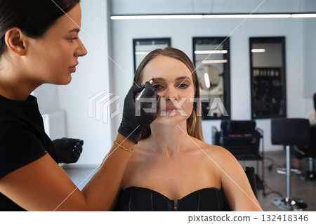 Makeup artist applies makeup to client in professional studio setting during a beauty session Makeup artist applies makeup to client in professional studio setting during a beauty session 132418346