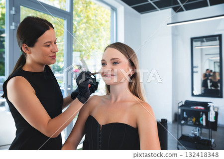 Makeup artist applies cosmetic enhancement to client inside a bright beauty salon during a sunny afternoon Makeup artist applies cosmetic enhancement to client inside a bright beauty salon during a sunny afternoon 132418348