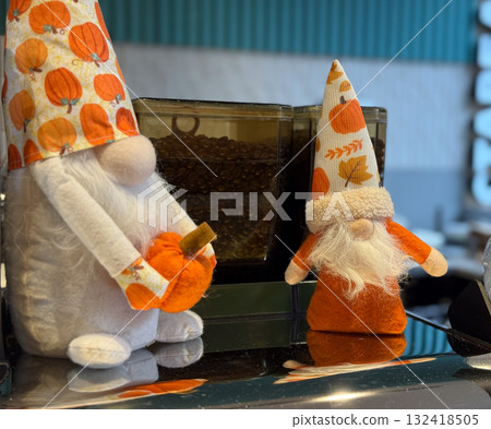 Two autumn gnome decorations with pumpkin patterns and white beards. Cozy seasonal display, festive cafe atmosphere and warm handcrafted charm celebrating the spirit of fall. 132418505