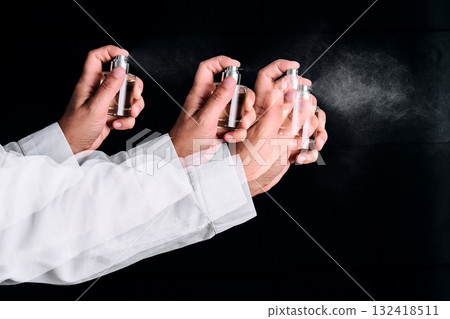 A hand in a white shirt sprays perfume or air freshener. Black background. 132418511
