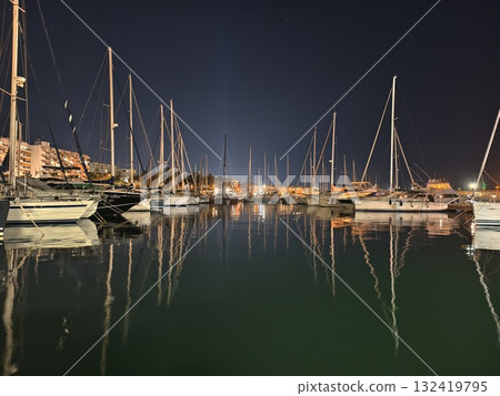 peaceful harbor with mirrored sailboats and twinkling lights creating serene nautical atmosphere peaceful harbor with mirrored sailboats and twinkling lights creating serene nautical atmosphere 132419795