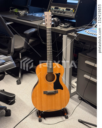 Acoustic guitar standing in modern recording studio. Musical creativity, artistic inspiration and sound production atmosphere with instruments and audio equipment. 132419855