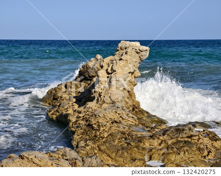 mythic landscape featuring animallike eroded rock against vibrant azure horizon with foamy surf 132420275