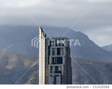 industrial concrete against mountains, rugged mountain ridges contrast sharply with concrete spire industrial concrete against mountains, rugged mountain ridges contrast sharply with concrete spire 132420368