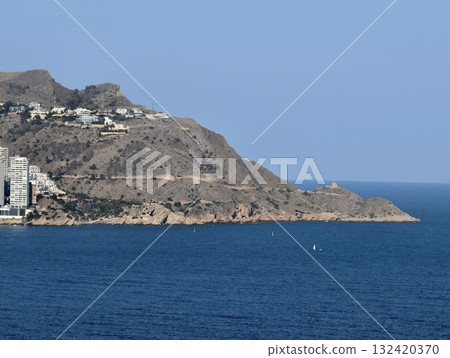 picturesque hillside village on sunlit coastline overlooking serene blue sea and rocky shore 132420370