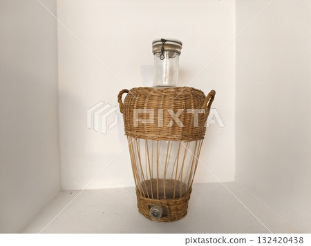 woven basket holding aged glass demijohn, vintage wicker demijohn bottle in rustic setting woven basket holding aged glass demijohn, vintage wicker demijohn bottle in rustic setting 132420438