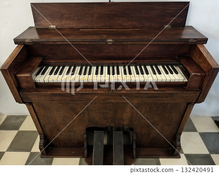 old upright piano with worn features, vintage upright piano showing years of use and silent history 132420491