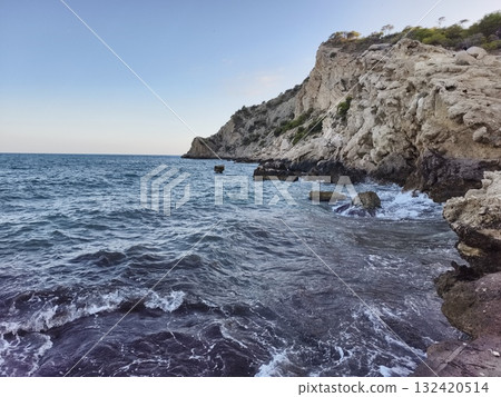 calm sea with rocky shoreline, peaceful coastal landscape with gentle ripples and warm sunlight 132420514