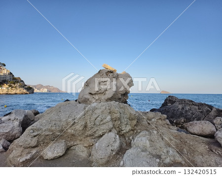 serene sea with textured stone foreground, quiet horizon featuring rugged rock formations and smooth 132420515