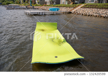 Kids having fun on a floating mat in the lake during a sunny summer day near cozy lakeside houses Kids having fun on a floating mat in the lake during a sunny summer day near cozy lakeside houses 132420599
