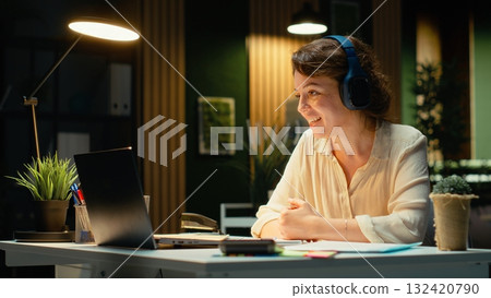Focused consultant takes notes during executive board meeting video call, extracting essential bullet points from the discussion with business associates. Late night briefing session. Camera B. 132420790