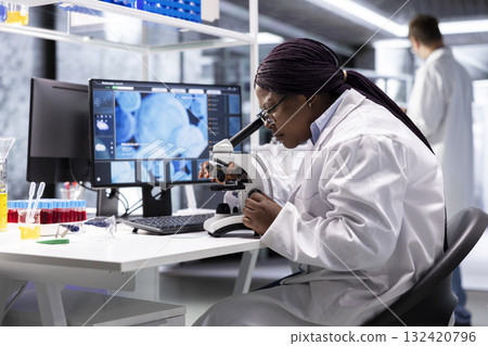 Black scientist examining samples under microscope in a modern laboratory. Research work integrates biotechnology, molecular science and advanced diagnostics to shape medical discovery. 132420796