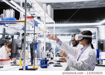 Laboratory chemical engineer using virtual reality tech to process DNA patient data for clinical research. Lab worker wearing VR goggles gear to do genetic analysis diagnostics Laboratory chemical engineer using virtual reality tech to process DNA patient data for clinical research. Lab worker wearing VR goggles gear to do genetic analysis diagnostics 132420820